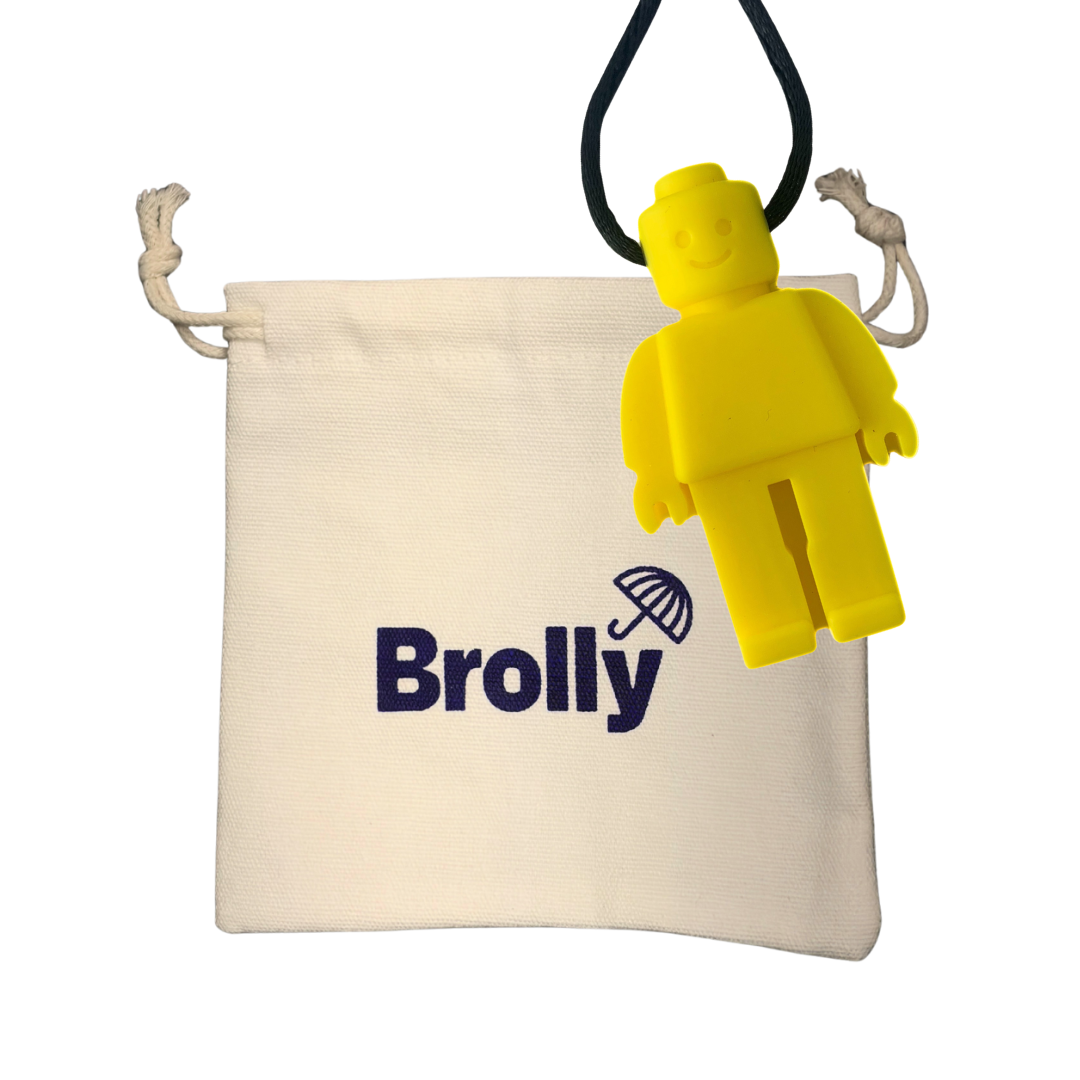 Beige drawstring pouch and robot-shaped Brolly Sheet Chew Necklace on a black cord against a white background - Yellow