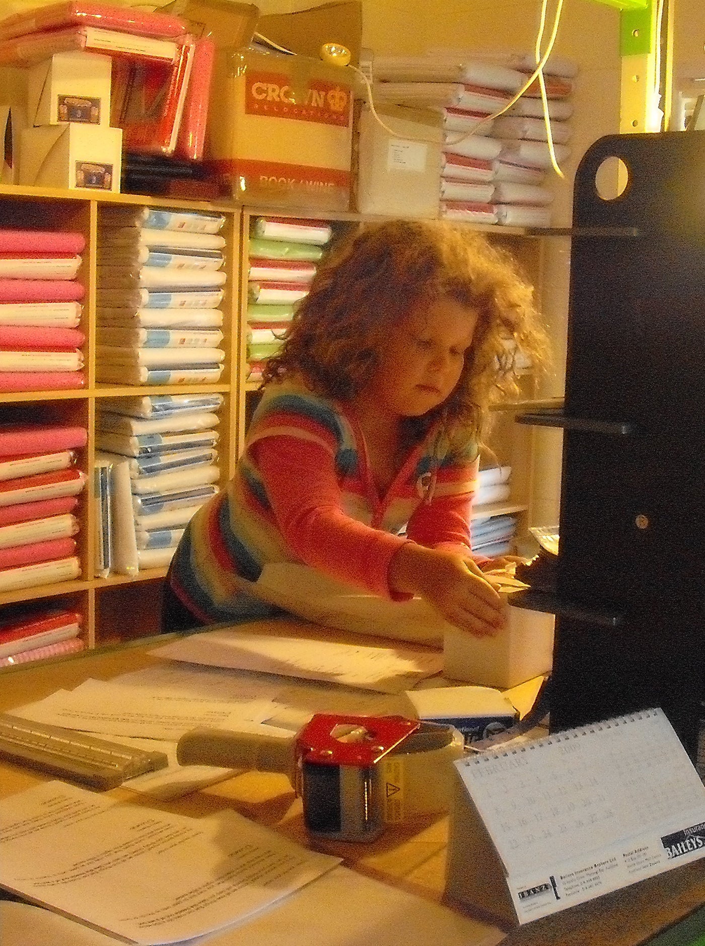Colour picture of young Mia packing orders in the spare room.  In the background are cubes full of Brolly Sheets waiting to be ordered