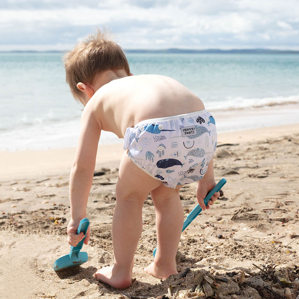 Child wearing a colorful nappy on a beach - Narwhales