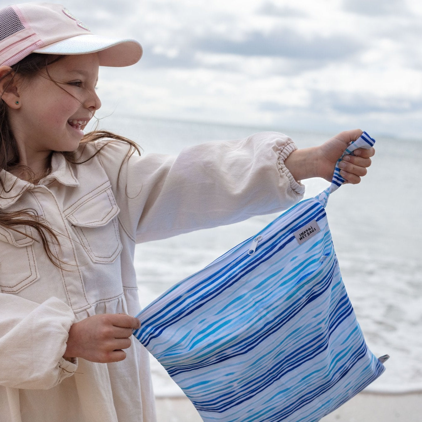 Child holding a A Snazzi Pants Wet Bag - Double in Ocean Print on a beach with ocean in the background