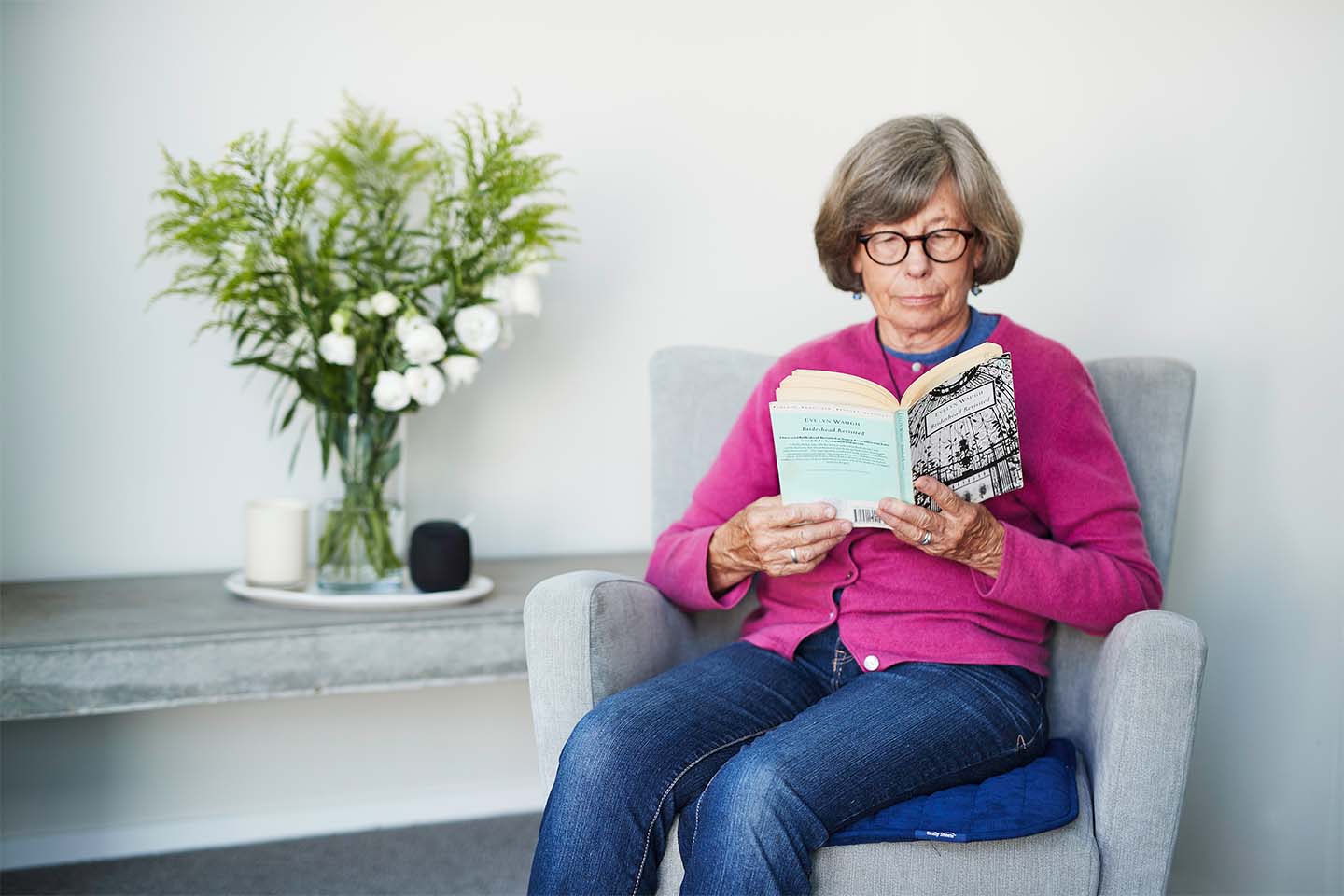 Women reading a book on a grey chair with a blue chair pad