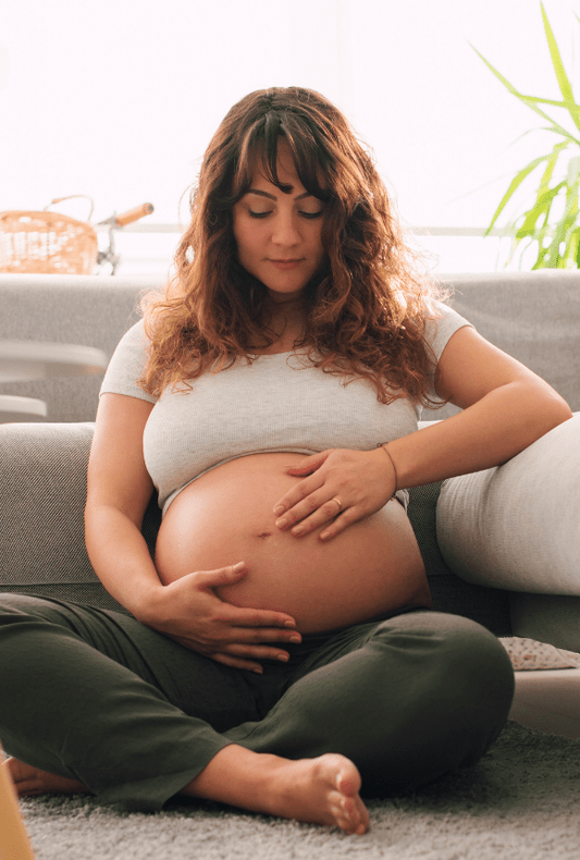 Pregnant Woman sitting on the floor in her lounge holding her pregnant belly