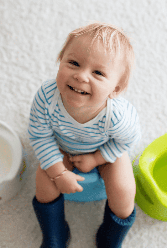 Smiling toddler sitting proudly on top of his potty, with two other potties on either side of him.