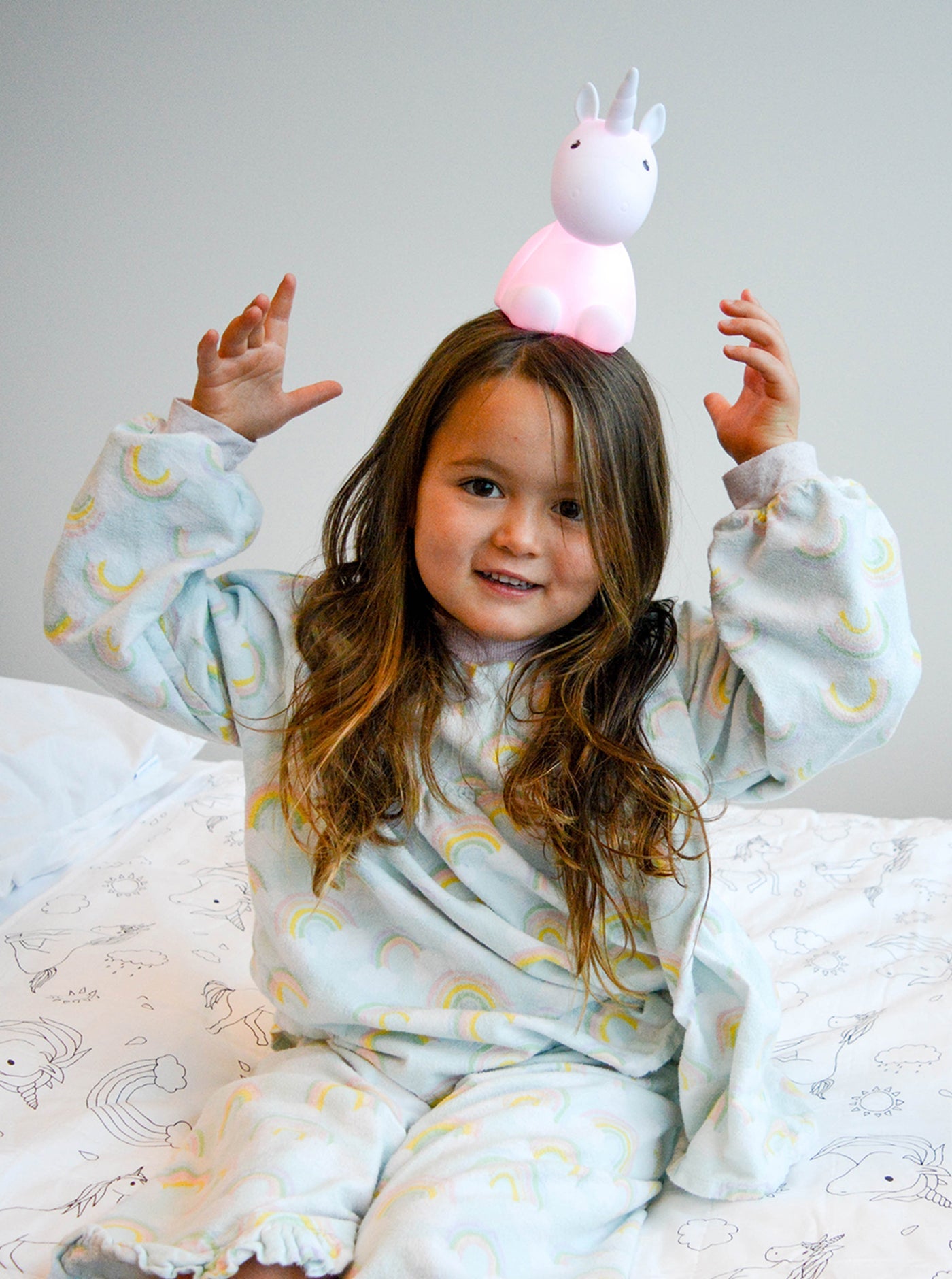 Girl in pyjamas sitting on Unicorn Brolly Sheet with balancing Unicorn night light on her head