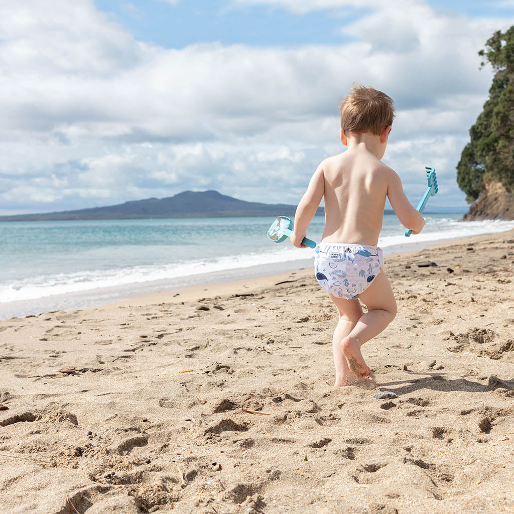 Child wearing a colorful nappy on a beach - Narwhales