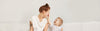Baby holding Mum's nose and laughing against a plain white backdrop